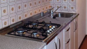 A kitchen with white cabinets, a gas stove, a stainless steel sink, and patterned backsplash tiles. - Nice three-bedroom flat with balcony in Bibione (Bibione)