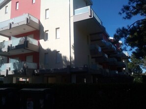 Um edifício residencial com várias andares, varandas, fachada vermelha e branca, e um céu claro.