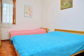 A bedroom with two beds, a window with curtains, and a wall with two framed pictures. - Cozy two-room flat 100mt from Bibione beach (Bibione)