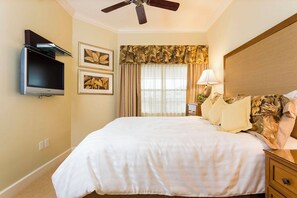 Quarto de hotel com cama, ventilador de teto, televisão na parede e janela com cortinas.