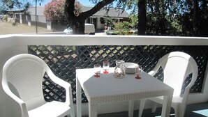 Een terras met twee witte plastic stoelen en een tafel, een wit hek en een boom met roze bloemen.