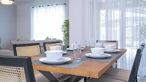 Zona pranzo con tavolo in legno apparecchiata per quattro persone, circondata da sedie in vimini.