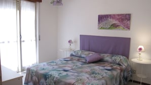 A bedroom with a bed, a nightstand, a lamp, a painting, and a window with curtains. - Modern flat at Grado Pineda (Grado Pineta)