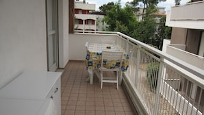 A balcony with a tiled floor, a table with a patterned tablecloth, and a chair. - Modern flat at Grado Pineda (Grado Pineta)
