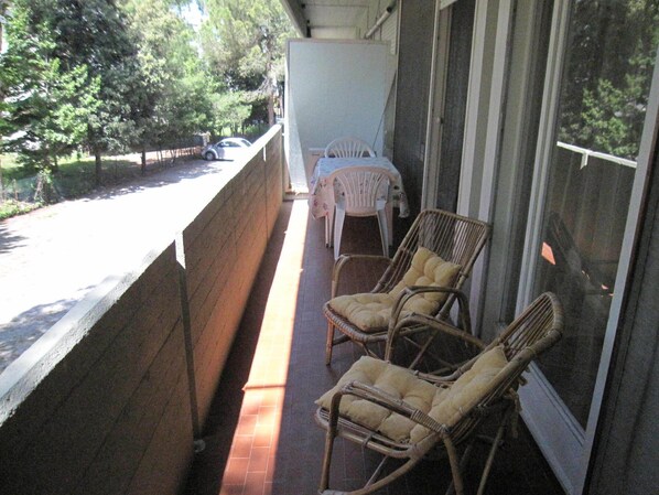 Un balcon avec des fauteuils en osier, une table et une vue sur une rue et des arbres.