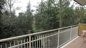 A balcony with a white railing, a yellow table, and a view of a forested area. - Nice and cozy flat at Grado Pineta (Grado Pineta)
