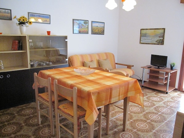 A dining area with a table set for two, a sofa, and a television on a stand.