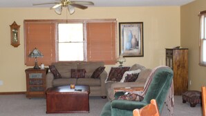 A living room with a ceiling fan, a sofa, a green armchair, a wooden coffee table, and a lamp.