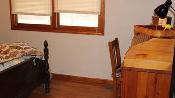 A bedroom with a wooden bed, a desk with a lamp, and a window with blinds.