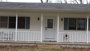 A single-story house with a white exterior, a front door, and a small porch with a white railing.