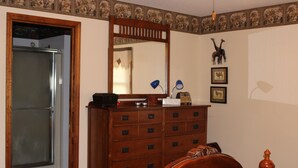 A bedroom with a wooden dresser, a bed with patterned bedding, a mirror, and wall-mounted animal pictures.