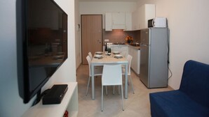 Eine kompakte Küche mit Esstisch, Stühlen, einem Kühlschrank und einem an der Wand montierten Flachbildfernseher.
