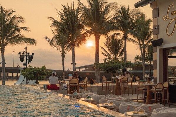 A poolside area with lounge chairs and tables, palm trees, and a sunset in the background. - Venice Hotel Phu Quoc (Phu Quoc)