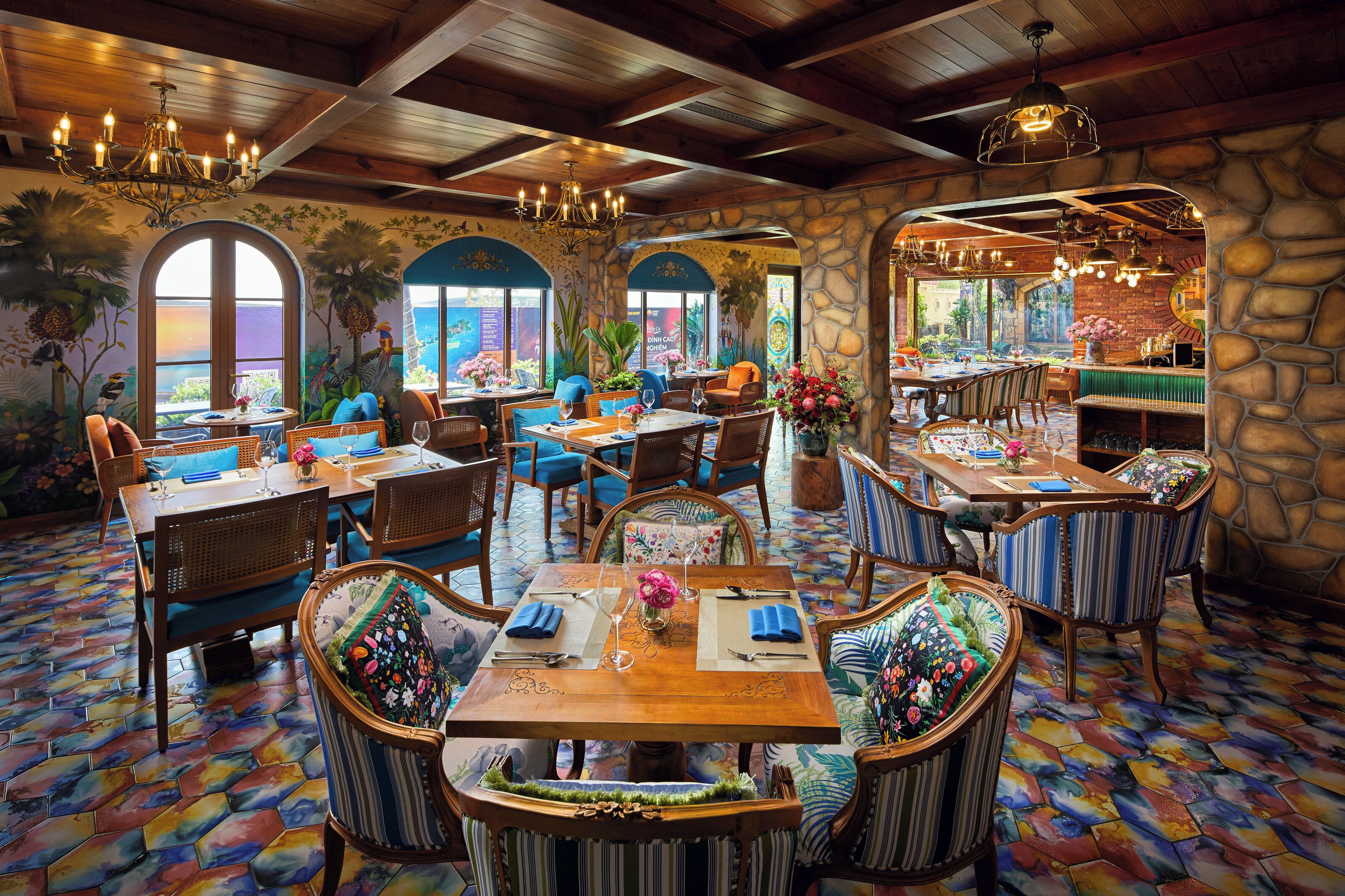 A restaurant with wooden tables and chairs, stone walls, and colorful tiled floors.
