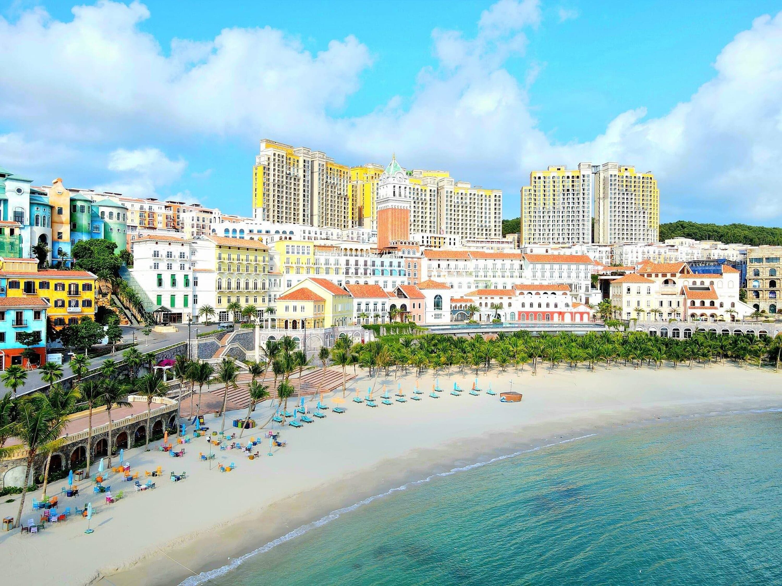 A coastal cityscape with a beach, colorful buildings, and a clear sky.