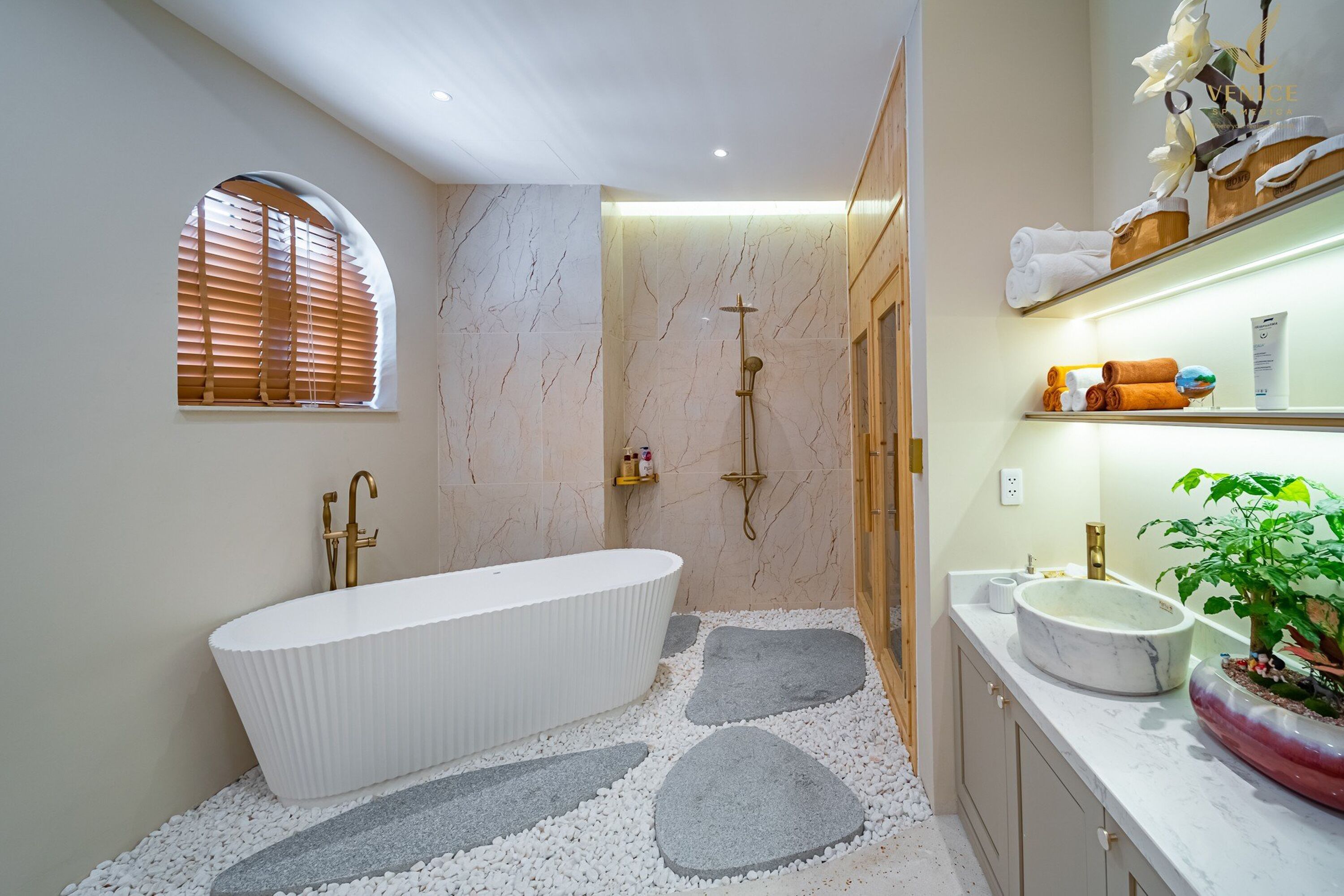 A modern bathroom with a freestanding bathtub, a walk-in shower, and a vanity with a large sink and a potted plant.