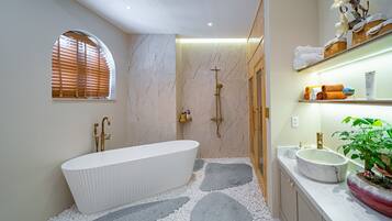 A modern bathroom with a freestanding bathtub, a walk-in shower, and a vanity with a large sink and a potted plant.