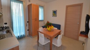 A compact kitchen with a stove, a dining table with two chairs, a wooden cabinet, and a door.