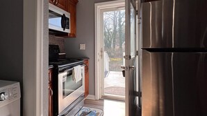 A kitchen with a stainless steel refrigerator, oven, and microwave, wooden cabinets, and a view through an open door to an outdoor deck. - Large 2 bedroom | Queen beds | Safe Area (Hampton)