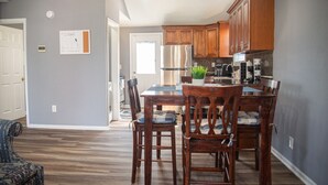 A modern kitchen with wooden cabinets, a stainless steel refrigerator, and a dining area with a table and chairs. - Large 2 bedroom | Queen beds | Safe Area (Hampton)