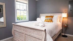 A bedroom with a wooden bed, a window, a bedside lamp, and a mirror on the wall. - Large 2 bedroom | Queen beds | Safe Area (Hampton)