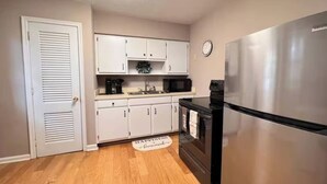 A compact kitchen with white cabinets, a stainless steel refrigerator, and a microwave. - Perfect for families! (Newport News)