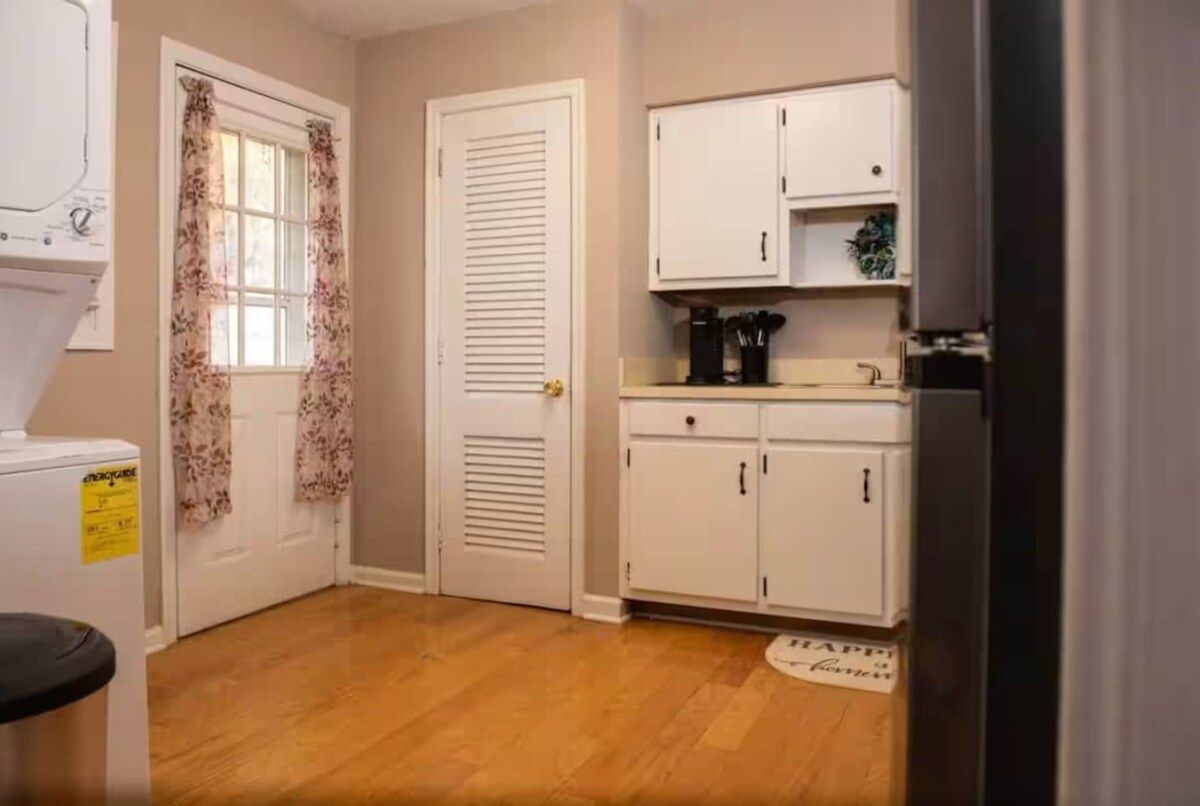 A compact kitchen with white cabinets, a coffee machine, and a window with floral curtains.