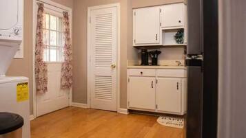 A compact kitchen with white cabinets, a coffee machine, and a window with floral curtains.