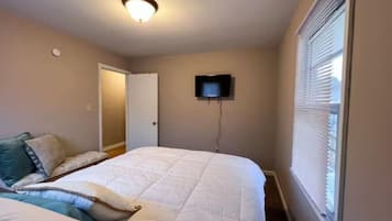 A bedroom with a bed, a television mounted on the wall, and a window with blinds.