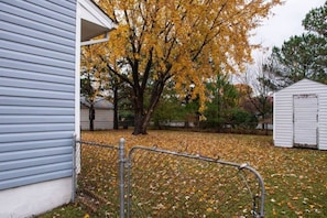 Ein Wohnhaus mit eingezäuntem Garten, einem Baum mit gelben Blättern und einem Gartenhaus.
