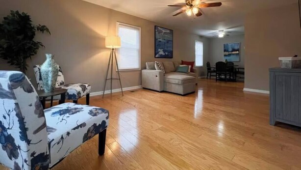 A spacious living room with hardwood flooring, a ceiling fan, a sofa, a coffee table, and a lamp. - Perfect for families! (Newport News)