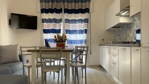 Une cuisine moderne avec des meubles blancs, un téléviseur à écran plat et un coin repas comprenant une table et des chaises.