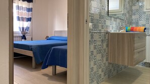Une chambre avec deux lits, une salle de bain avec un miroir et un lavabo, et une fenêtre avec des rideaux.