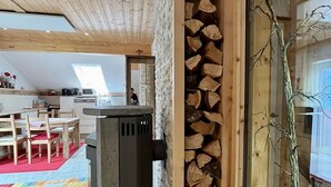 A cozy interior with a stone wall, a wood-burning stove, and a dining area with chairs and a table. - Ferienwohnung Smaragd in Herrlich, Sonniger Höhenlage mit Großglocknerblick (Heiligenblut)