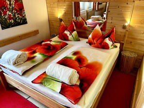 Una cama doble con ropa de cama estampada con motivos florales, un cabecero de madera y una mesita de noche pequeña con espejo.