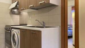 Una cocina compacta con armarios de madera, lavadora incorporada y pileta de acero inoxidable.