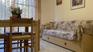 Una sala de estar con un sofá de madera, una mesa de comedor con sillas y un jarrón con flores.