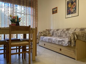 A living room with a wooden sofa, a dining table with chairs, and a vase with flowers.