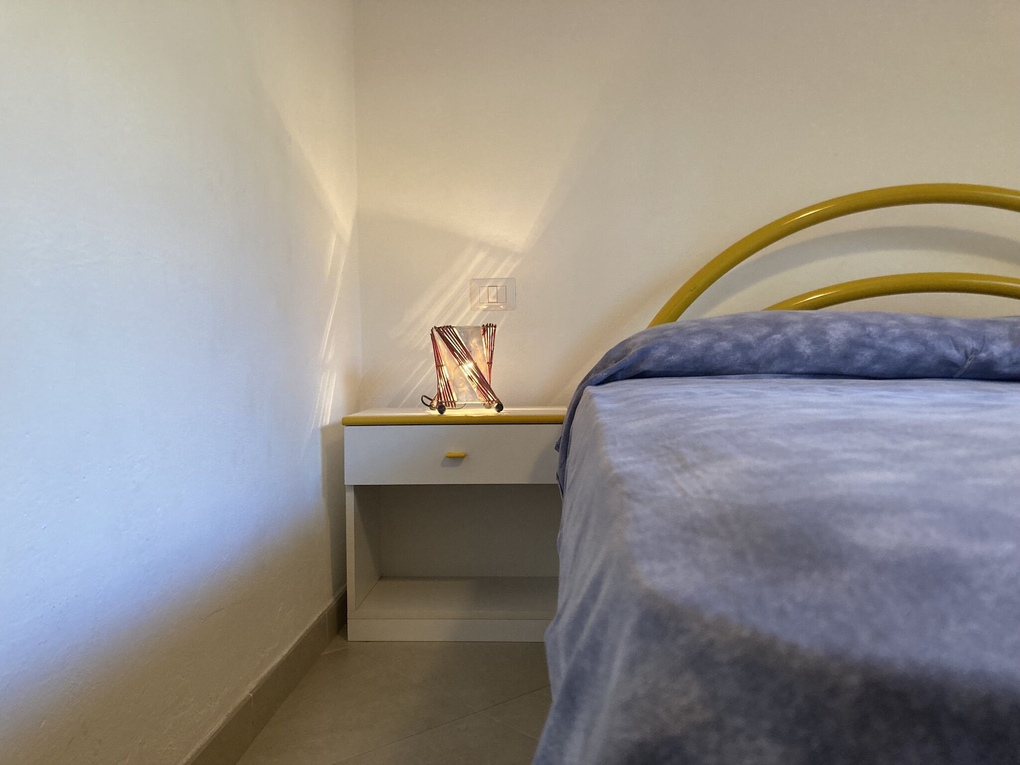 Ein kleines, ordentliches Schlafzimmer mit einem Bett, einem Nachttisch und einer Lampe.