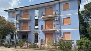 Un edificio residencial de varios pisos con balcones, unidades de aire acondicionado y una entrada con portón.