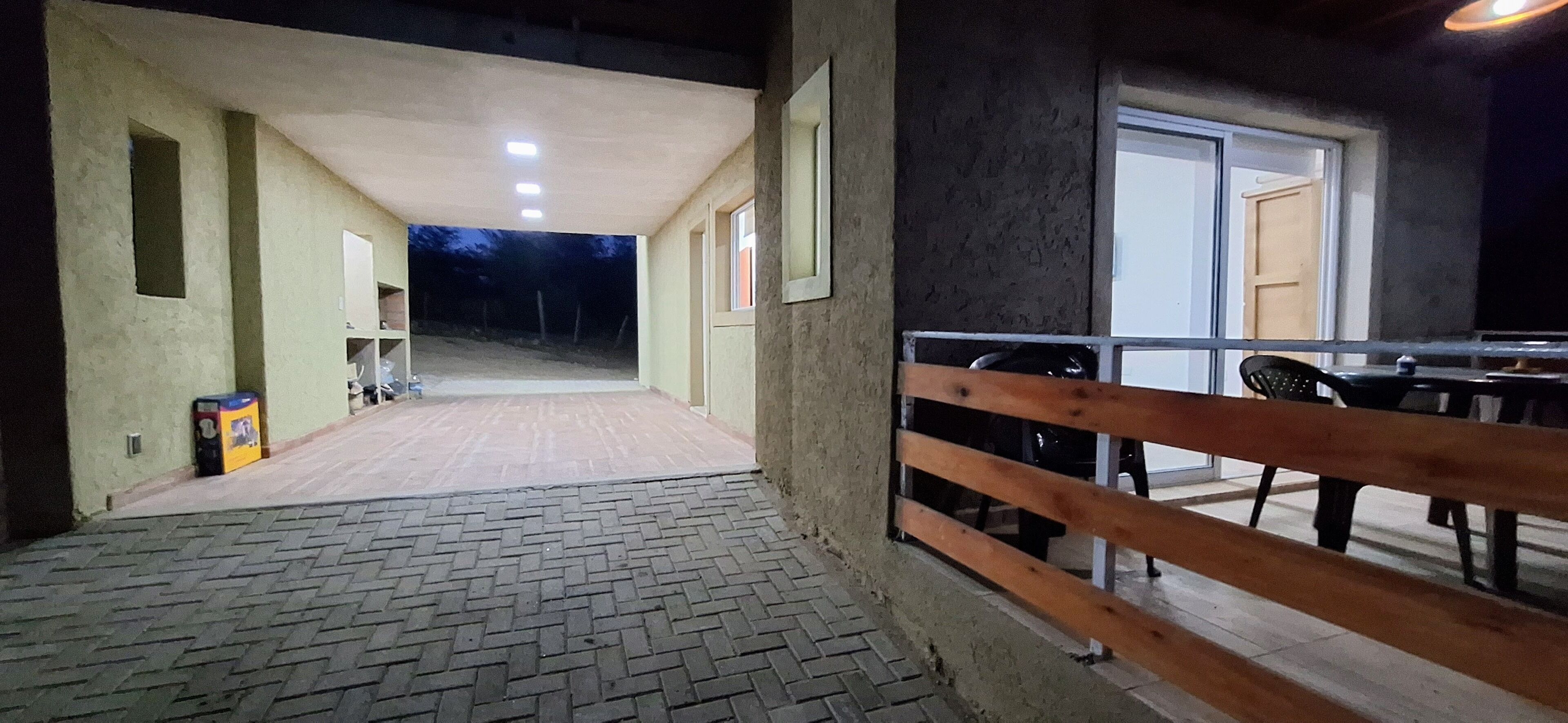 An indoor corridor with a brick floor, wooden railing, and a view of an outdoor area at night.