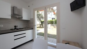 A modern kitchen with white cabinets, a gas stove, and a stainless steel range hood. There is a sliding glass door leading to an outdoor area.