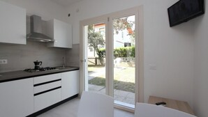A modern kitchen with white cabinets, a gas stove, and a stainless steel range hood. There is a sliding glass door leading to an outdoor area. - Wonderful villa with garden (Bibione)