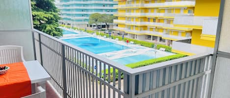 A balcony with a pool, white chairs, and a table with a fruit bowl.