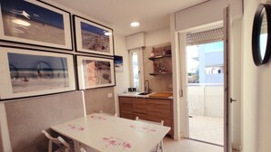 Una cocina compacta con zona de comedor, vistas a un balcón por una puerta abierta, y cuadros en la pared.