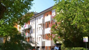 Un edificio residencial de varios pisos con balcones, rodeado de abundante vegetación y árboles.
