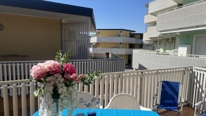Ein Balkon mit Tisch, gedeckt für eine Mahlzeit, mit Blumen in einer Vase und einer blauen Tischdecke.