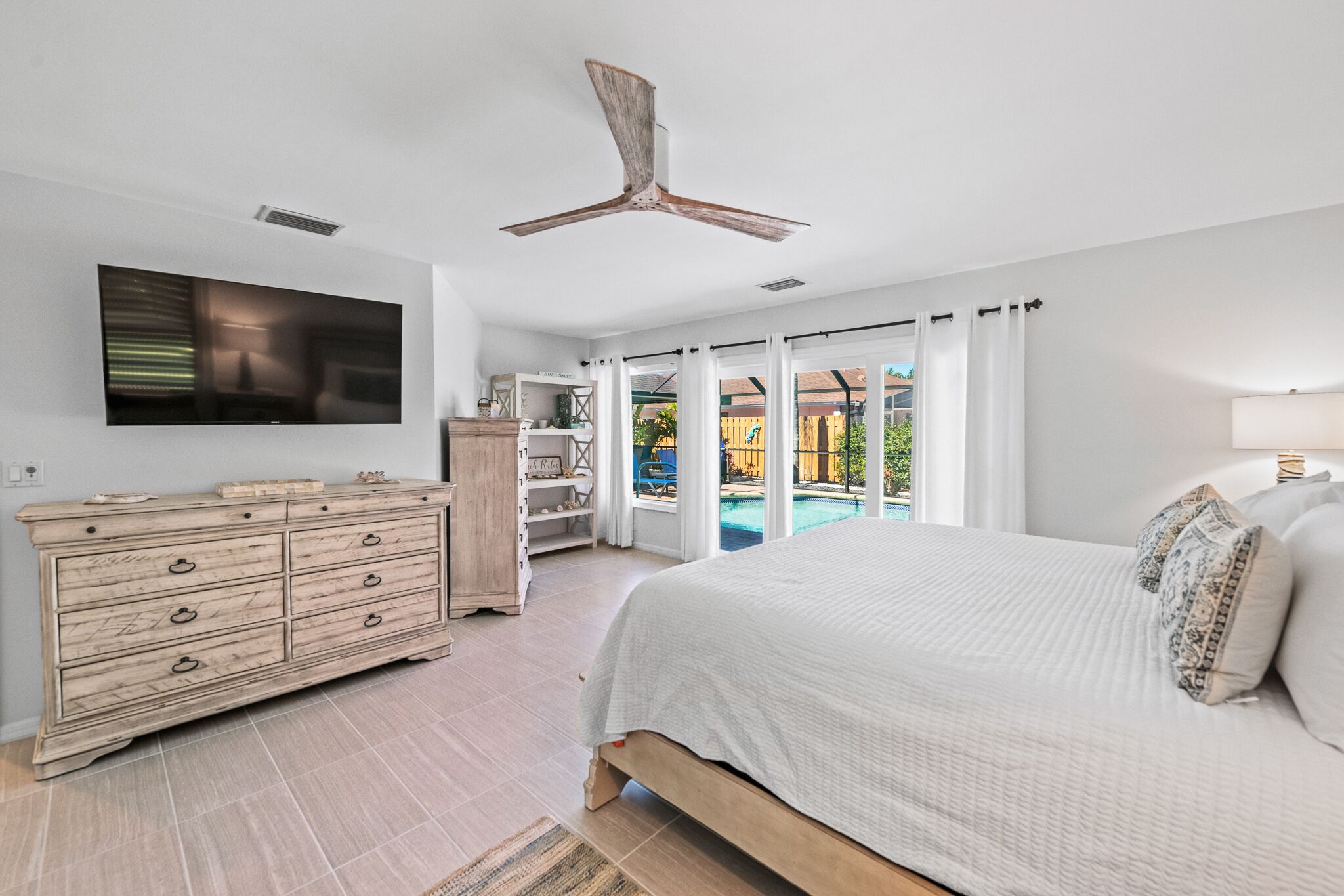 A bedroom with a large bed, a wooden dresser, a flat-screen TV, and a ceiling fan.