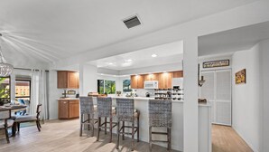 Uma cozinha moderna com armários de madeira, uma ilha central com banquetas e uma área de jantar com mesa e cadeiras.