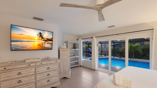 Quarto com uma grande janela com vista para uma piscina, um ventilador de teto e uma cômoda de madeira.